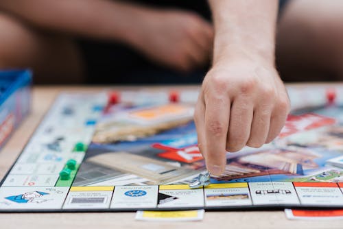 A person plays Monopoly, the famous board game, moving a piece across the board indoors