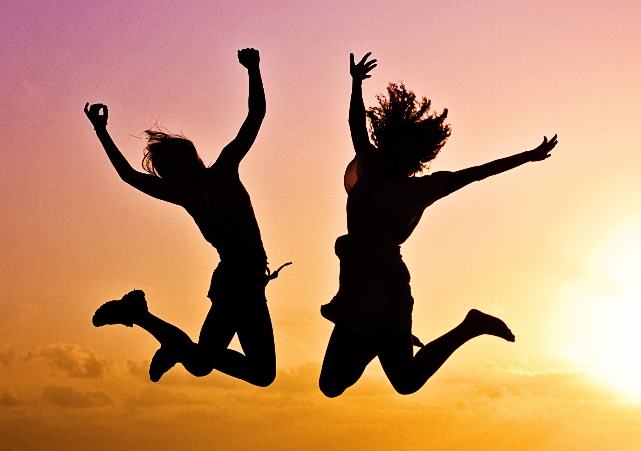 Silhouettes of two people joyfully jumping on a beach during a vibrant sunset