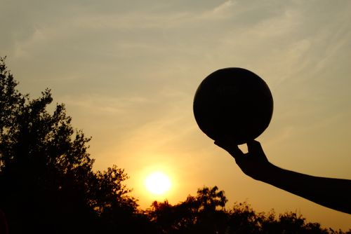 A silhouetted hand holding a ball against a vibrant sunset sky, creating a dramatic outdoor scene